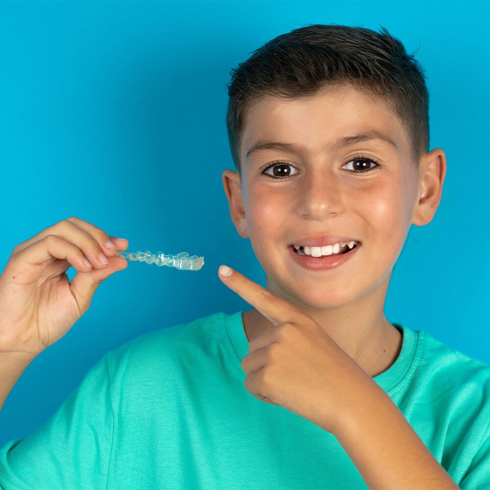 kid holding clear aligners and smiling